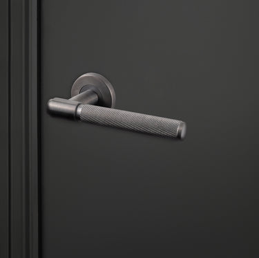 Moderne Lavuzo Cosenza deurklink Gun Metal met gekartelde greep op zwarte deur, rechteraanzicht