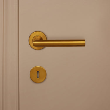 Mat gouden sleutelrozet Lavuzo rond gemonteerd onder gouden deurklink op beige deur, vooraanzicht