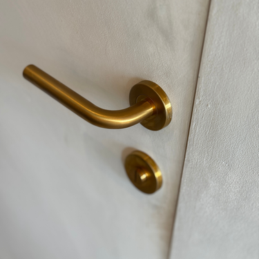 Oristano deurklink met PVD coating in het mat goud. sfeerbeeld op een lichtgekleurde deur