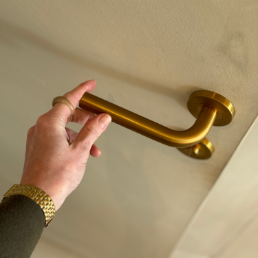 Een hand rijkt naar de Oristano mat gouden deurklink, sfeerimpressie van de warme uitstraling en dagelijks gebruik