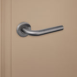 Elegant gebogen Gun Metal Oristano binnendeurklink van Lavuzo op beige achtergrond, linkeraanzicht