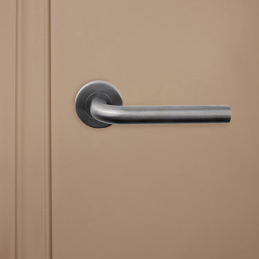 Lavuzo Oristano deurbeslag in Gunmetal PVD met ronde rozet op zandkleurige deur, vooraanzicht