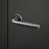 Oristano PVD gecoate deurkruk Gunmetal met rond rozet gemonteerd op zwarte deur, rechteraanzicht