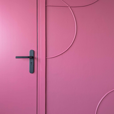 Deurklink zwart op schild op een knalroze deur met een roze wand voorzien van organische vormen